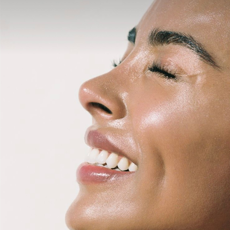 A close-up image of a person smiling, showing the lower part of their face with clear skin.