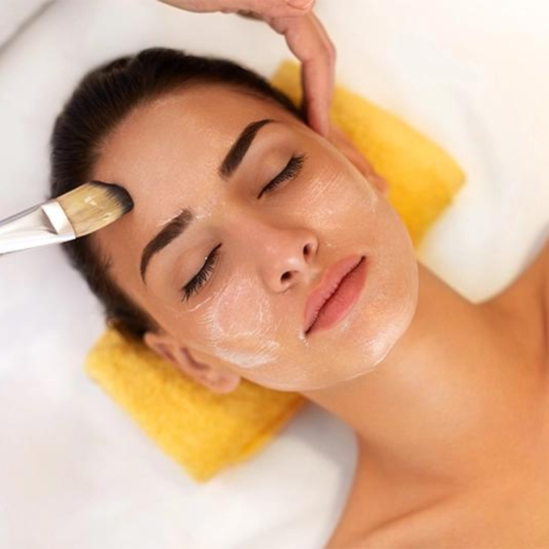 Woman receiving a facial treatment with a brush and towel on a white background